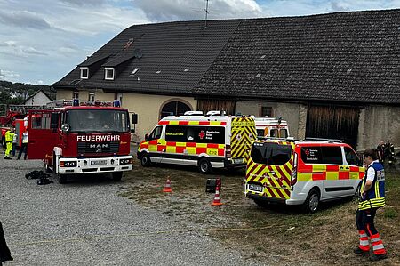 Einsatzfahrzeuge von BRK und Feuerwehr stehen vor einer Scheune