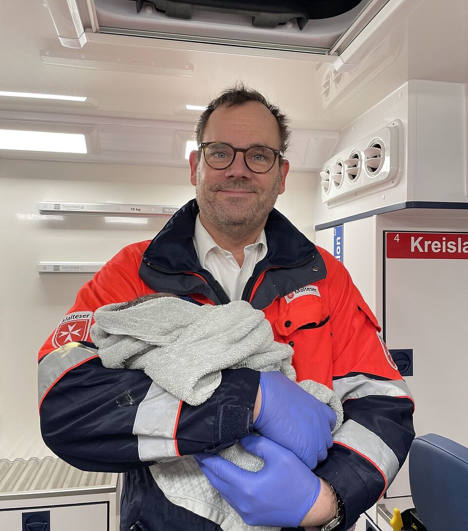 Notarzt Dr. Markus mit dem Neugeborenen auf dem Arm